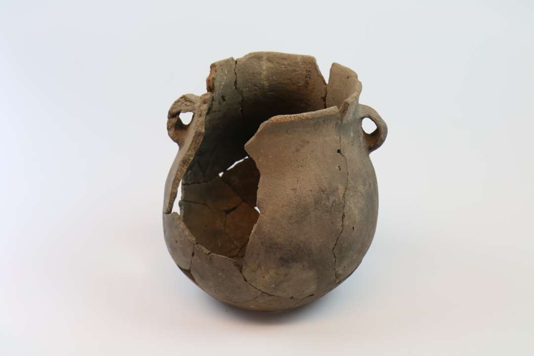 N�sten helt kar. �Rand: 13.5 cm.�Bug: 18 cm.�Bund: 9 cm.�H�jde 20 cm.�Randen er tynd og rundet. Overgang til bugen er j�vn. �2 cm under randen er  2 b�ndformede hanke (den ene er lidt deform, �den anden skaller af i den ene side).�Bunden buer en anelse indad. �Godset er fint, overfladen j�vn (skaller af flere steder).�Farve: Gr�brun. �Karret er sammensat. ��